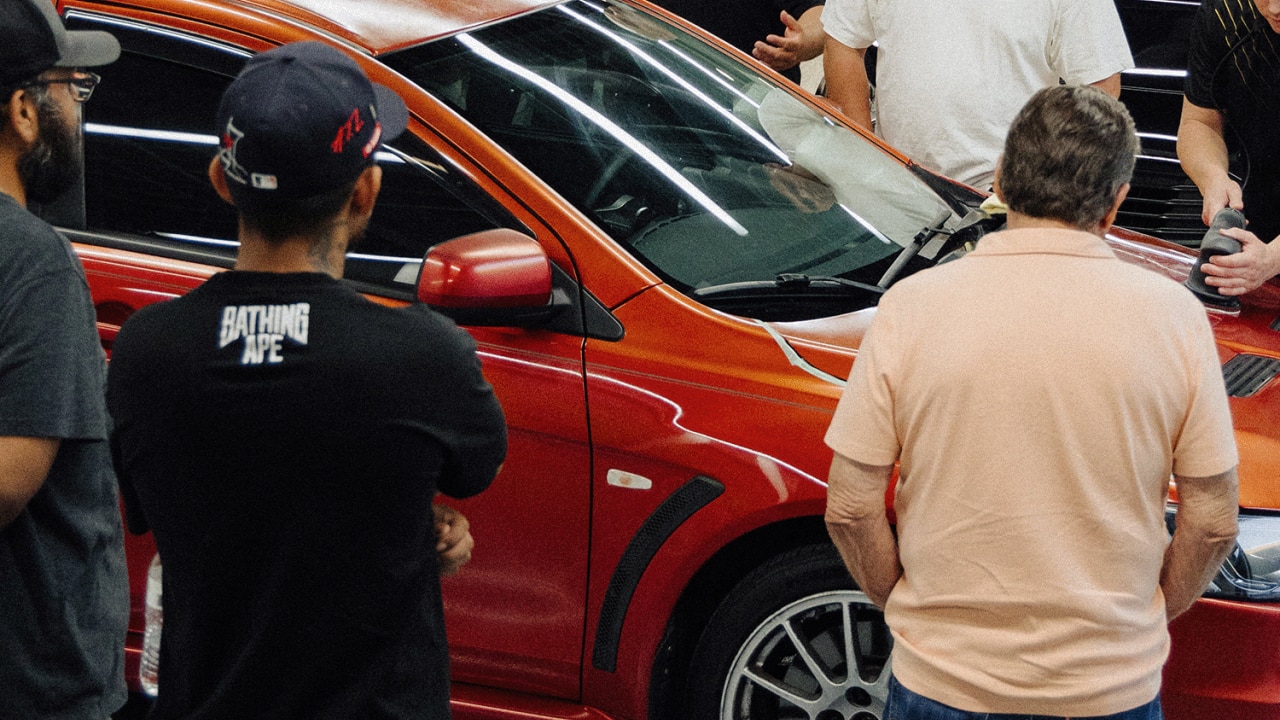 Several people standing around and looking at a clean and shiny red car