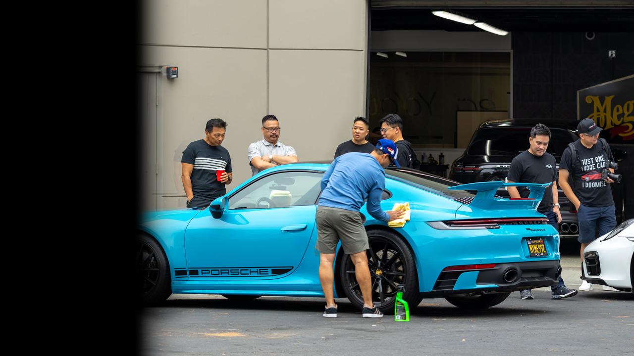 People standing around a blue sports car while one person is wiping it down.