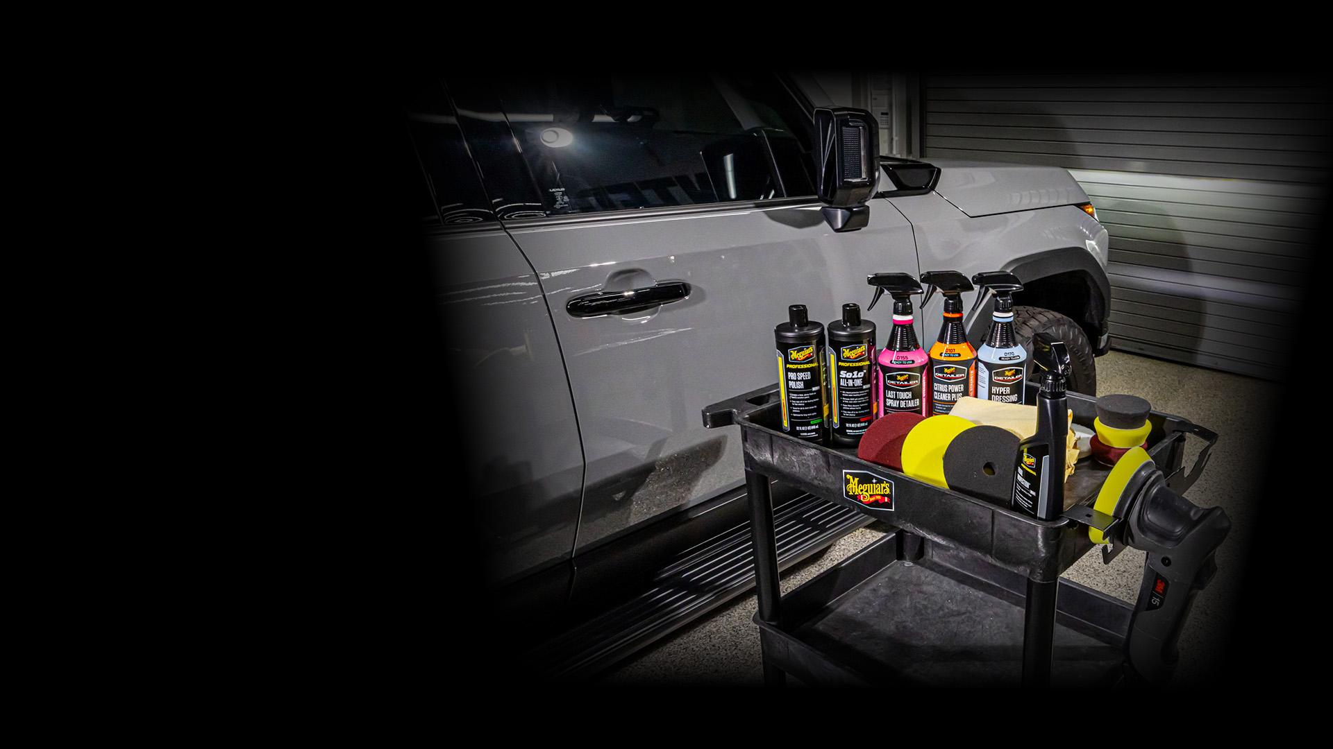 arious Meguiar's Professional products and pads displayed on a detailing cart in front of a gray SUV