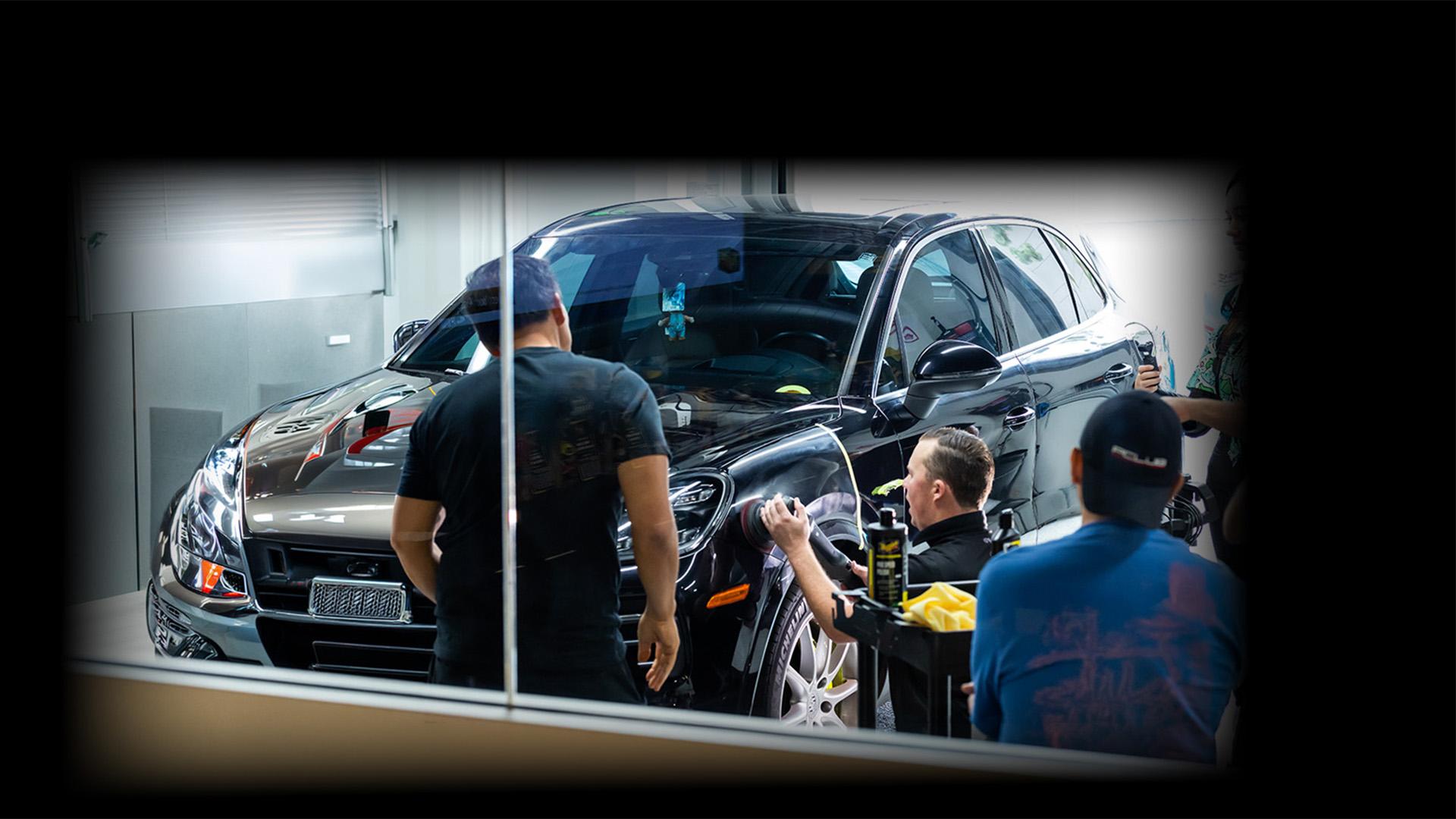 person buffing a front car panel with people watching