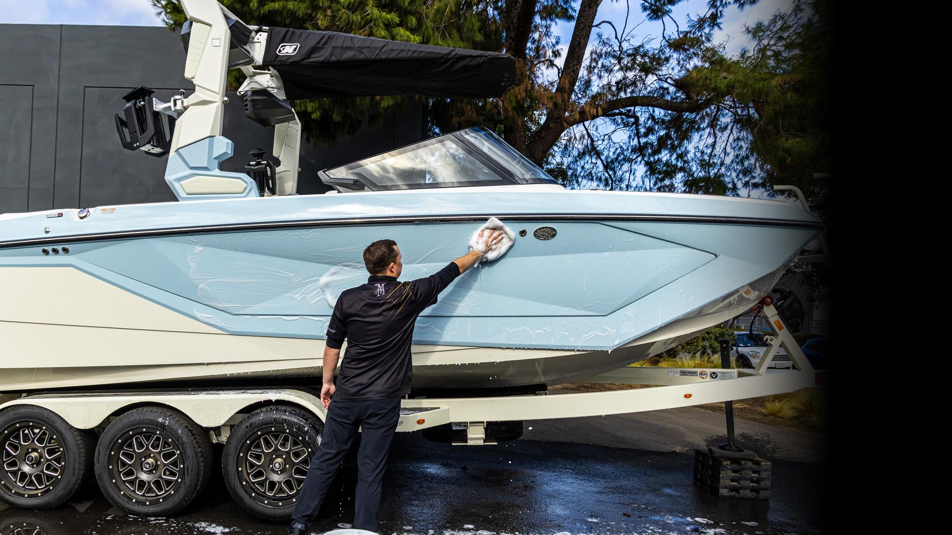 light blue and white motorboat mounted on a triple-axle trailer outdoors. The boat features sleek angular design elements, black wheels on the trailer, and a black canopy structure above the cockpit area.