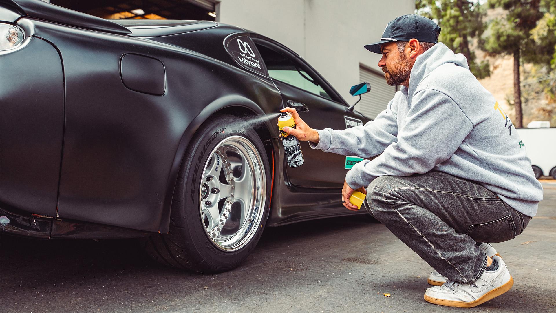 A person spraying a tire shine on to the tire of a black sports car