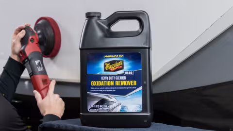 1 gallon bottle of Meguiar's Marine oxidation remover sitting in front of the side of a boat being worked on with a DA buffer