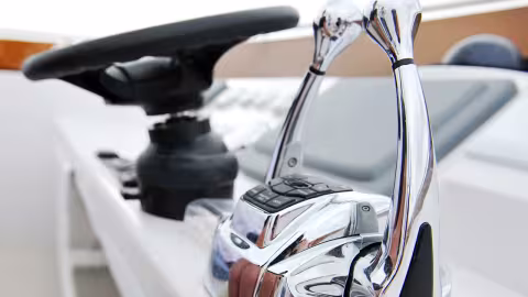 A close-up of a boat throttle control with two chrome levers and a steering wheel in the background.