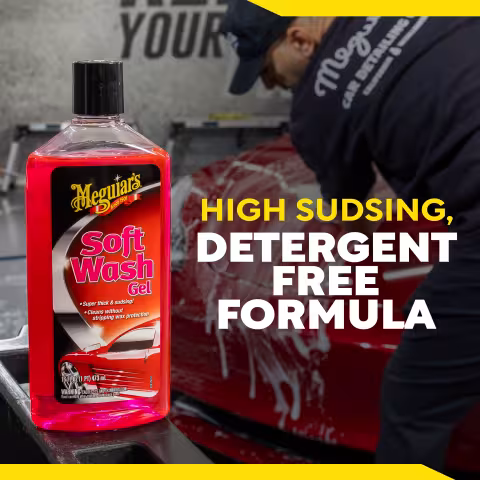 Meguiar’s Soft Wash Gel bottle displayed in the foreground with a red vehicle being washed in the background. Large text reads “HIGH SUDSING, DETERGENT FREE FORMULA.” The product label shows the brand Meguiar’s and product name Soft Wash Gel.